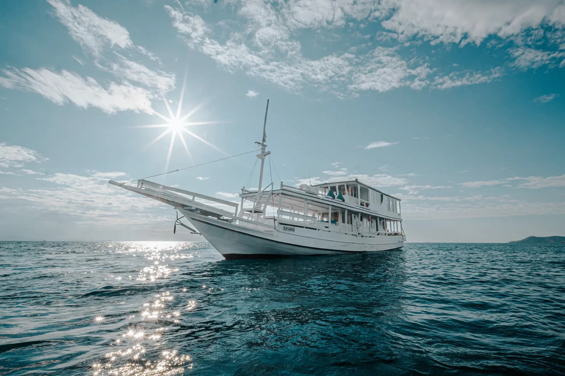 The Sabira liveaboard anchored at sea with a bright sun and reflection on the water's surface