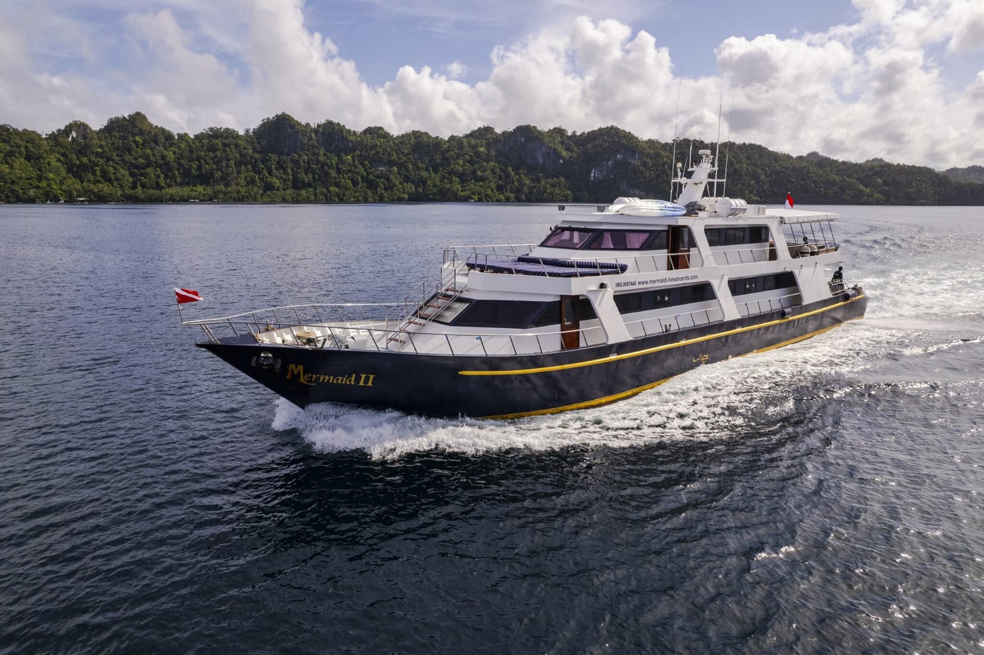 Mermaid II liveaboard cruising past forested islands, dark hull with a white superstructure